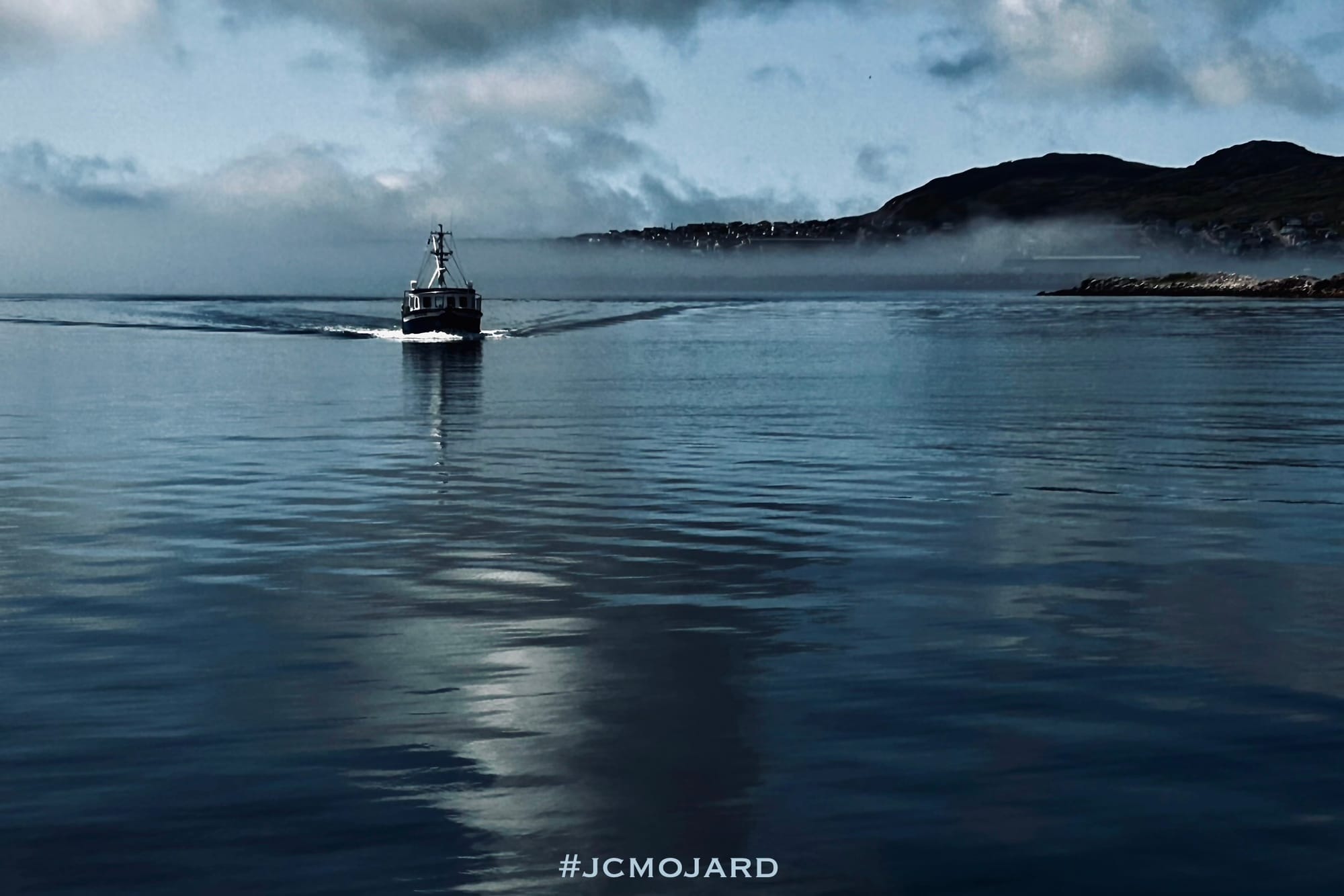 Un bateau sort d'un nuage de brume. Derrière lui, Saint-Pierre de Saint-Pierre-et-Miquelon.  