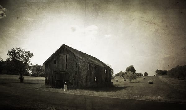 Une photo sépia d'une enfant fantomatique devant une maison en forme de grange qui tombe en ruine.